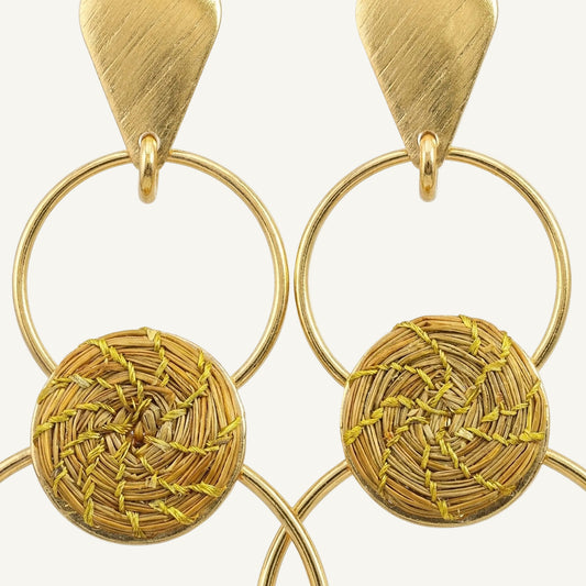 A pair of gold-toned statement earrings featuring a brushed triangular top, a thin circular hoop, and a round woven basketweave disc dangle on a white background.