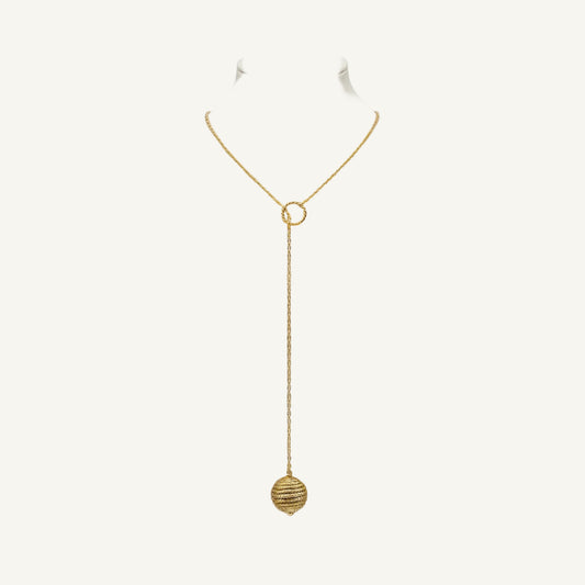 A gold lariat-style necklace with a textured circular ring at the collarbone and a dangling textured sphere pendant, displayed on a cream fabric mannequin bust against a white background.