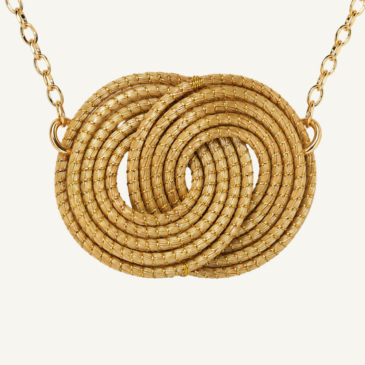 A gold necklace featuring a large, textured spiral pendant made of coiled mesh-like strands, suspended from a matching gold chain against a plain white background.