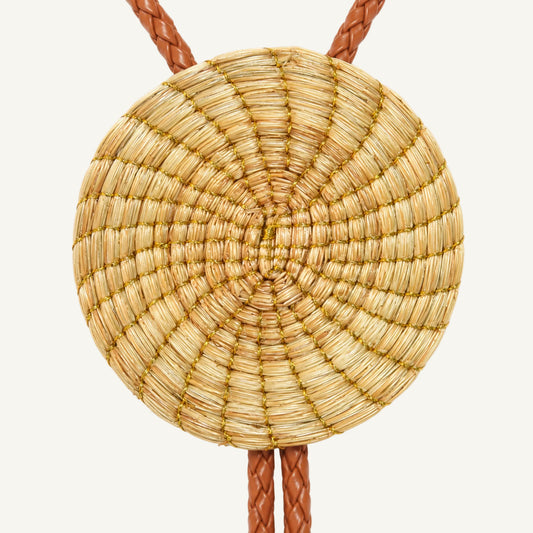 A round woven straw pendant necklace with a braided brown leather cord, shown against a plain white background.