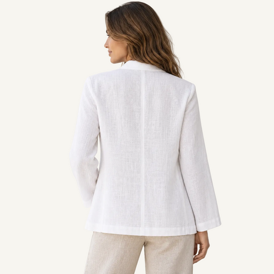 A woman shown from the back wearing a white linen long-sleeve blazer and light beige trousers, photographed against a neutral light beige studio background.