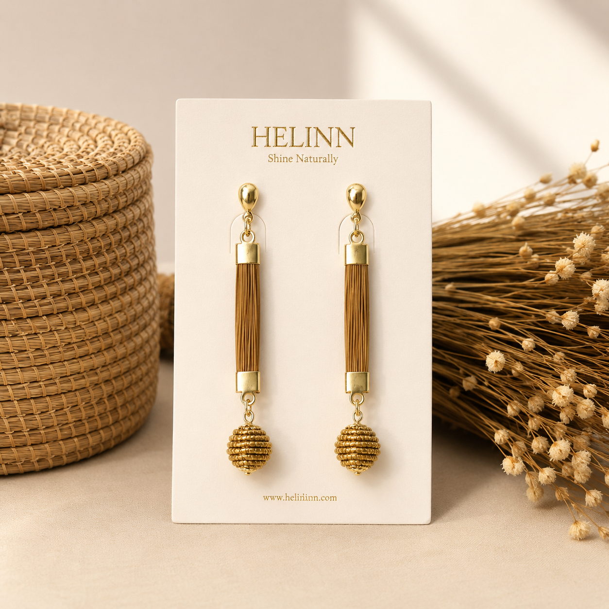 HELINN Alma Dourada handmade Golden Grass drop earrings displayed on natural woven background.