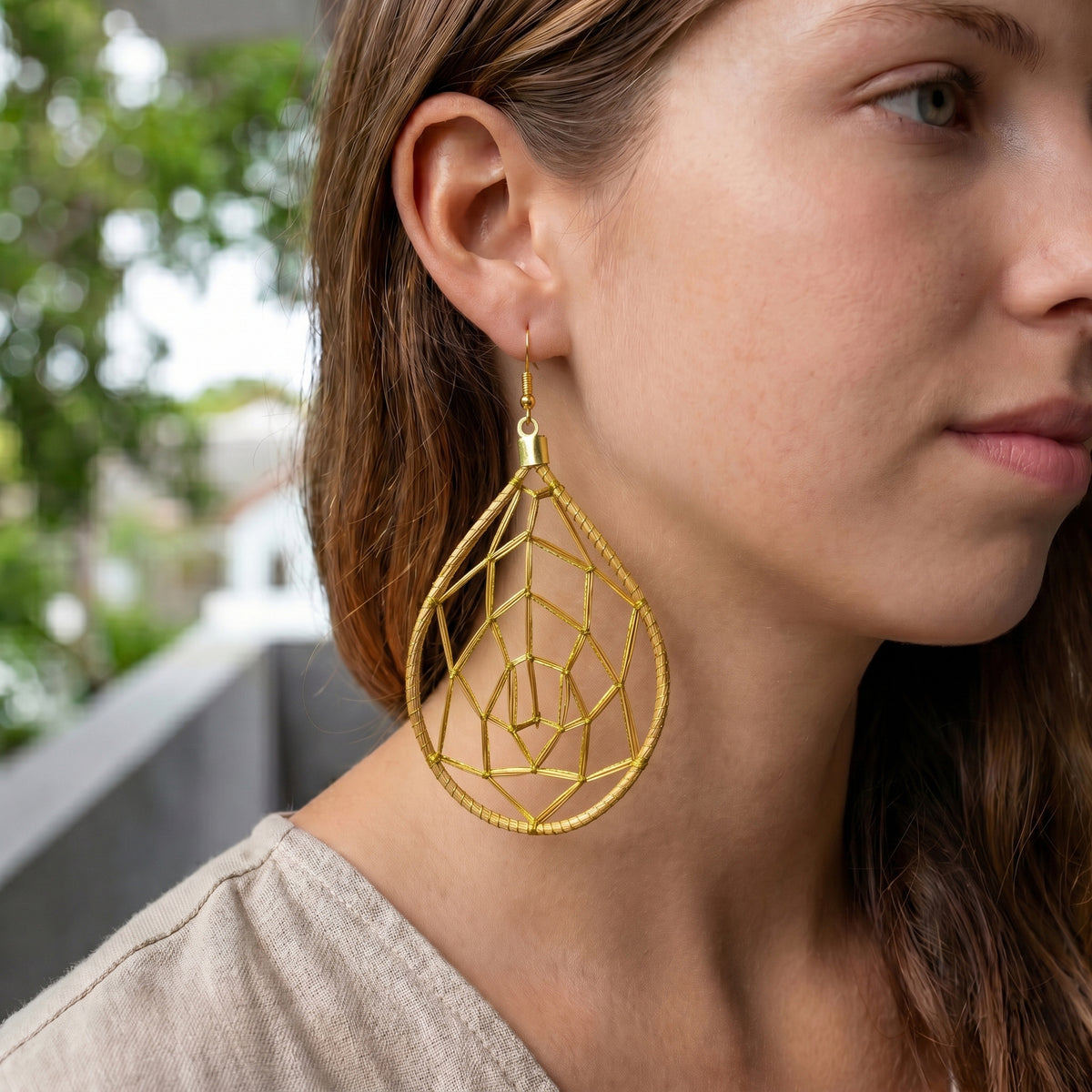 Close-up of a woman wearing gold geometric earrings with a blurred outdoor background