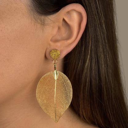 Woman wearing Aura Leaf Statement Earrings handcrafted with Brazilian Golden Grass and delicate gold botanical leaf pendant.