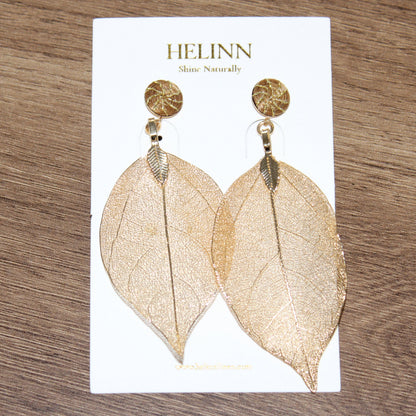 Woman wearing Aura Leaf Statement Earrings handcrafted with Brazilian Golden Grass and delicate gold botanical leaf pendant.