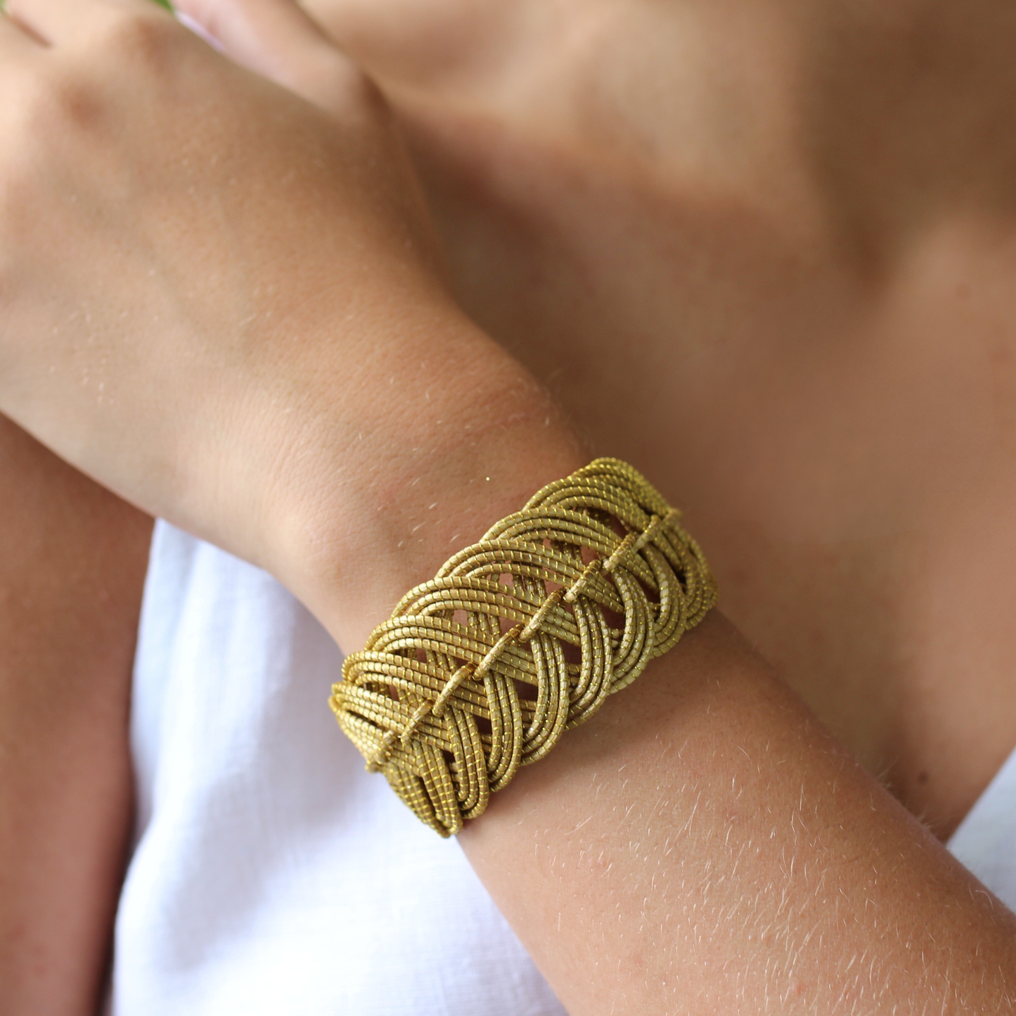 Gold braided bracelet on a wrist with a blurred background
