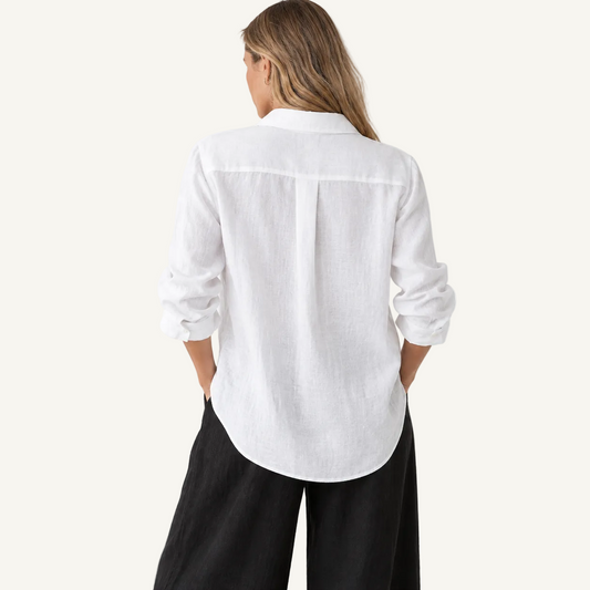 A woman shown from the back wearing a white long-sleeve linen button-up shirt and black wide-leg pants, set against a plain white studio background.