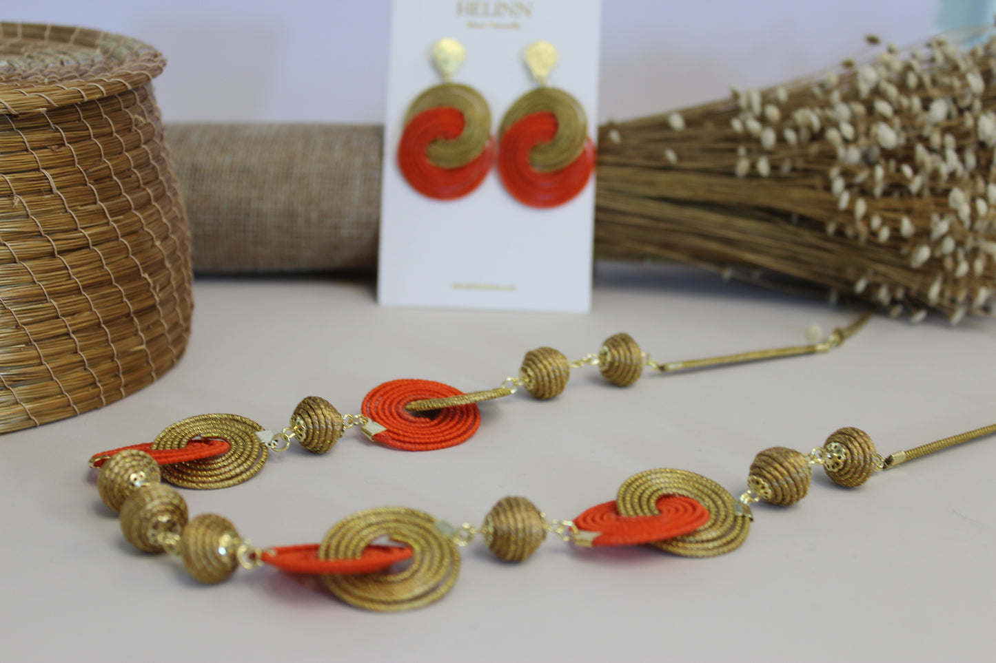 Necklace with red and gold accents on a light surface, with earrings in the background.