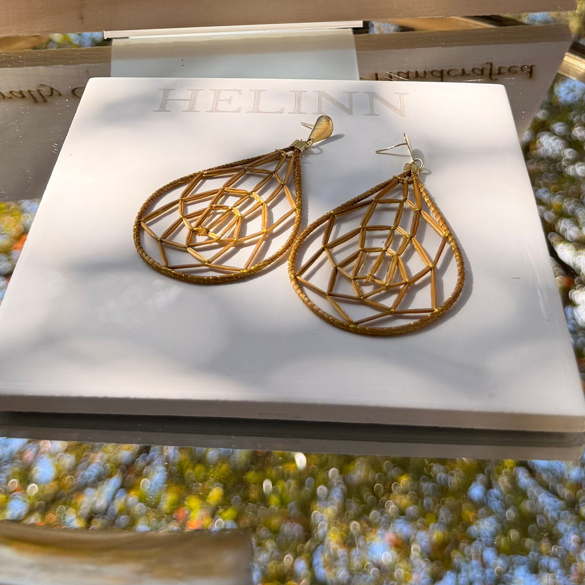 Gold earrings on a stand with 'Golden Grass' branding against a natural background.