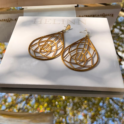 Gold earrings on a stand with 'Golden Grass' branding against a natural background.
