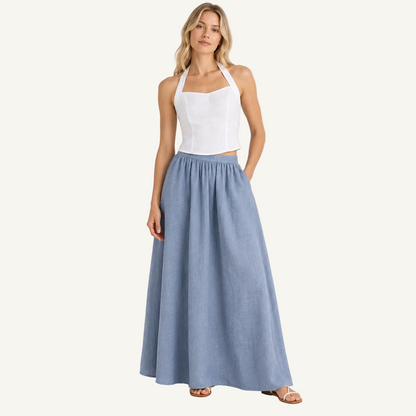A woman modeling a white sleeveless halter crop top and a high-waisted, flowing light blue linen maxi skirt against a plain white studio background.
