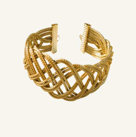 Gold bracelet on a white surface with a blurred natural background