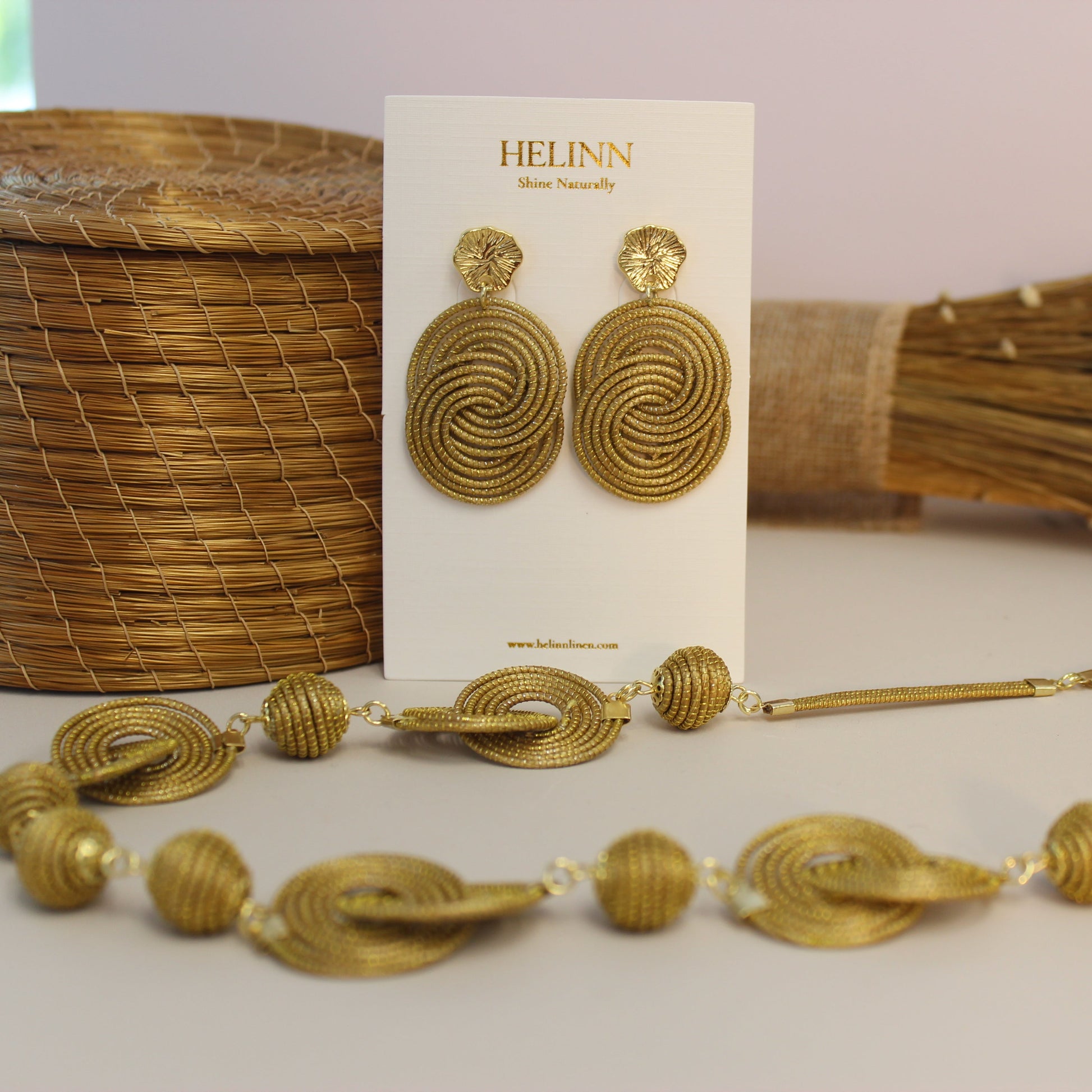 Gold necklace and earrings on a card with 'HELIINN' branding, placed on a light surface with a textured background.
