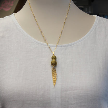 Handcrafted from Brazilian Golden Grass with premium 18K gold-plated details, the Aura Long Gold Drop Necklace features elegant woven spheres and a flowing tassel for timeless sophistication.