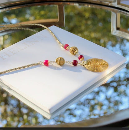 Handmade golden grass necklace with pink stones and circular woven pendant on white background by HELINN