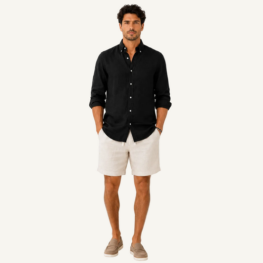 A man modeling a black long-sleeve button-up shirt and light beige linen shorts, paired with taupe slip-on shoes, against a plain white studio background.