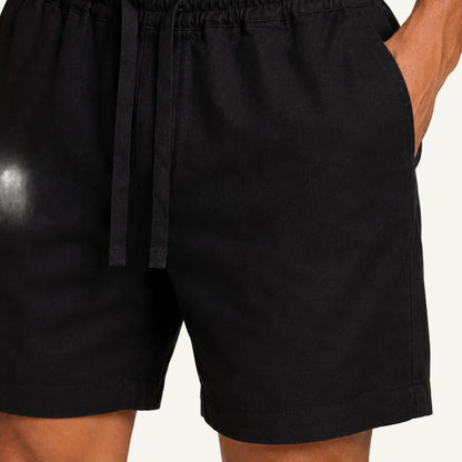 Close-up of a person wearing black drawstring linen shorts with side pockets, showing the waistband, fabric texture, and part of the leg against a light neutral background.