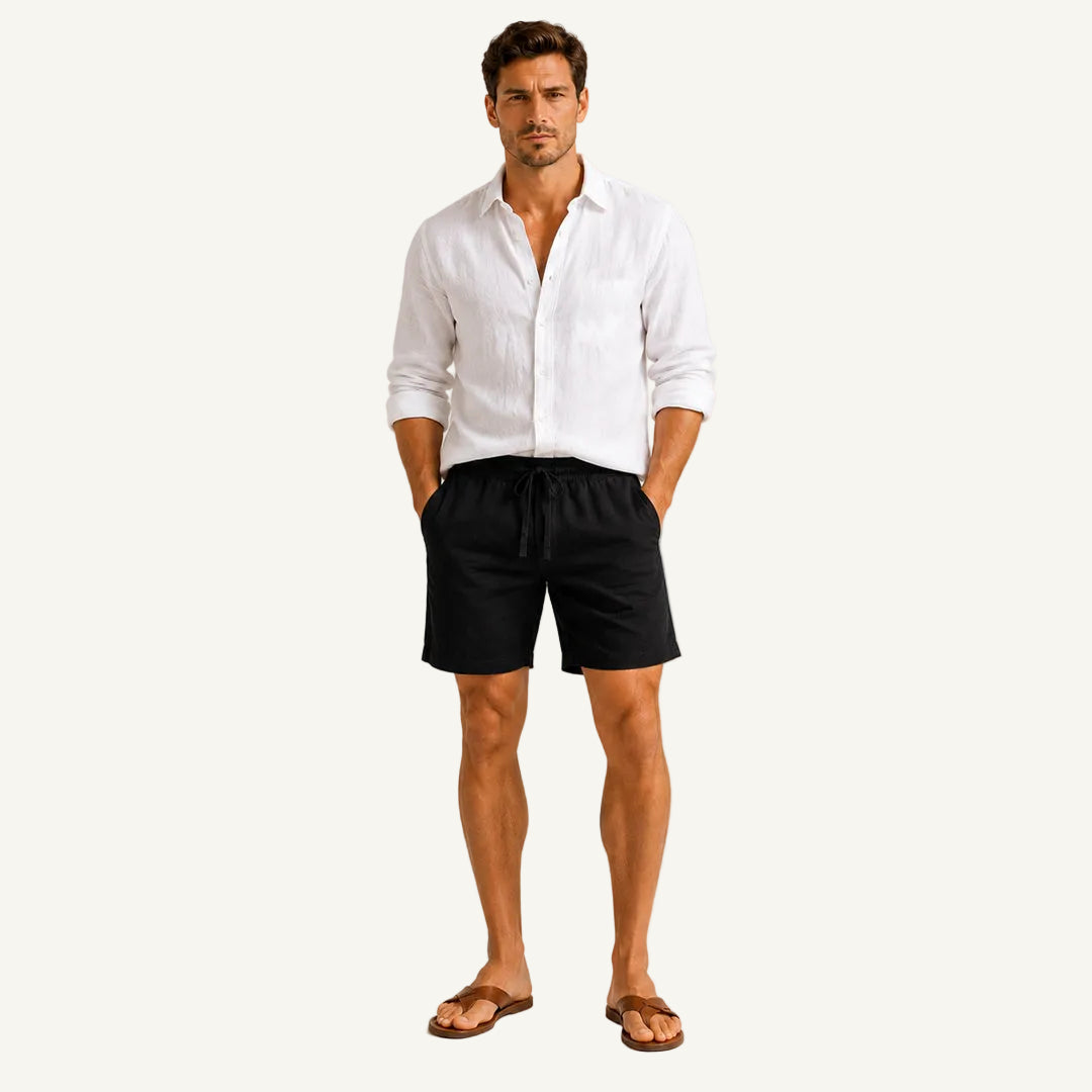 A man modeling a white long-sleeve linen shirt and black drawstring shorts against a light gray studio background.