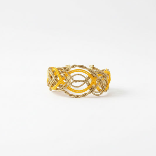 Sol Dourado golden grass bracelet cuff by HELINN displayed on white marble surface with natural woven decor