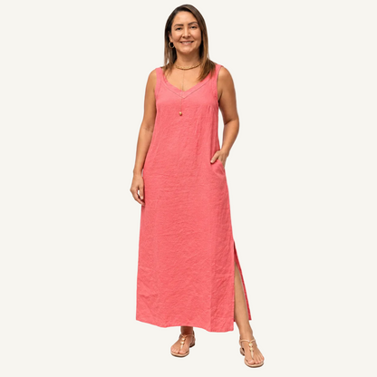 A woman modeling a sleeveless coral pink maxi dress with a V-neckline, side pockets, and a front slit, photographed against a clean white studio background.