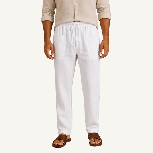 A person wearing loose white drawstring pants with side pockets, paired with a light beige shirt and brown sandals, standing against a plain beige studio background.
