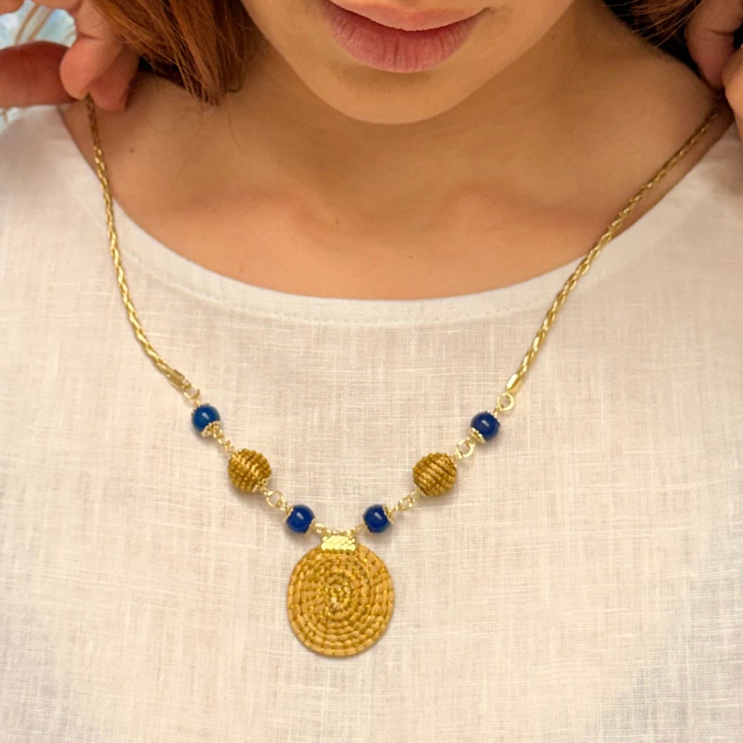 Woman wearing a gold necklace with blue beads on a plain background