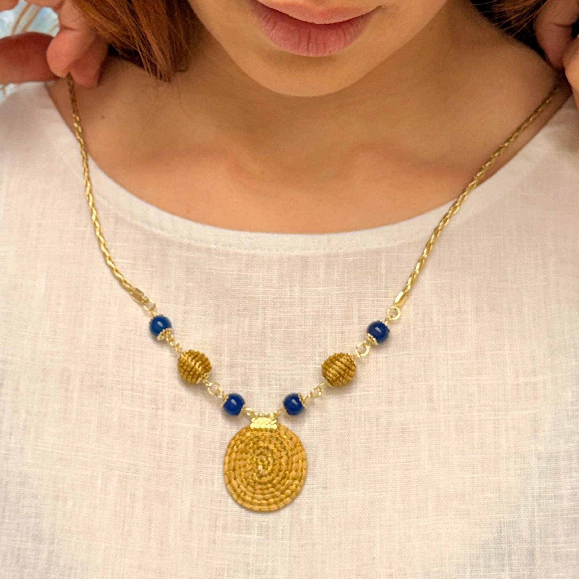 Woman wearing a gold necklace with blue beads on a plain background