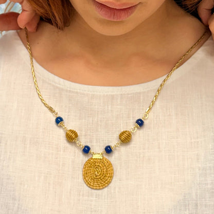 Woman wearing a gold necklace with blue beads on a plain background