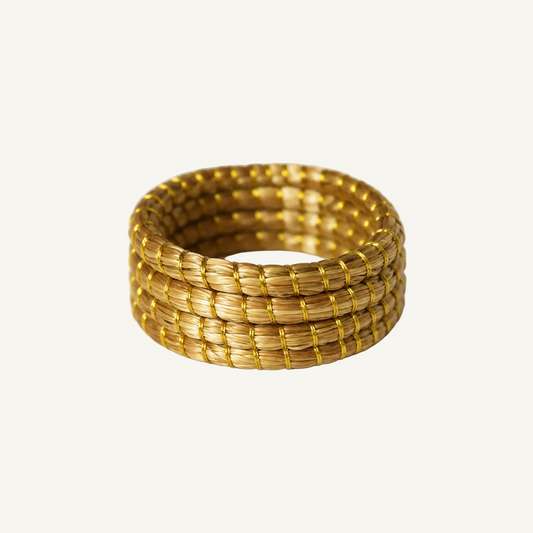 A wide, woven gold ring made from tightly wrapped strands, photographed on a clean white textured surface.
