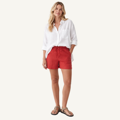 A woman modeling a white button-down shirt and red drawstring shorts against a clean white studio background.
