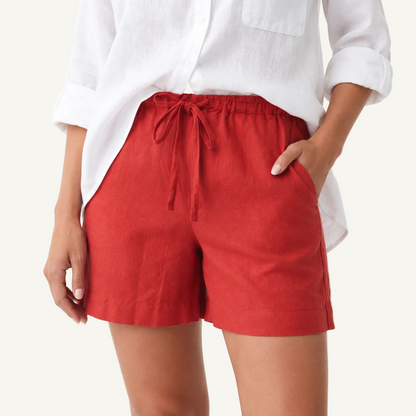 A person wearing bright red drawstring shorts and a white button-up shirt, shown from the chest to mid-thigh against a clean white studio background.