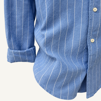 Close-up of a blue long-sleeve button-up shirt with thin white vertical pinstripes, showing the fabric texture, rolled cuff, and buttons against a plain light background.