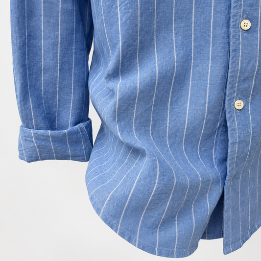 Close-up of a blue long-sleeve button-up shirt with thin white vertical pinstripes, showing the fabric texture, rolled cuff, and buttons against a plain light background.