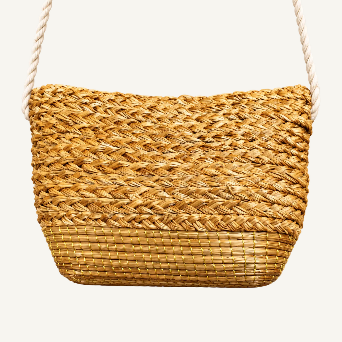 A woven straw shoulder bag with a natural tan color and a thick white rope strap, shown against a solid light beige background.