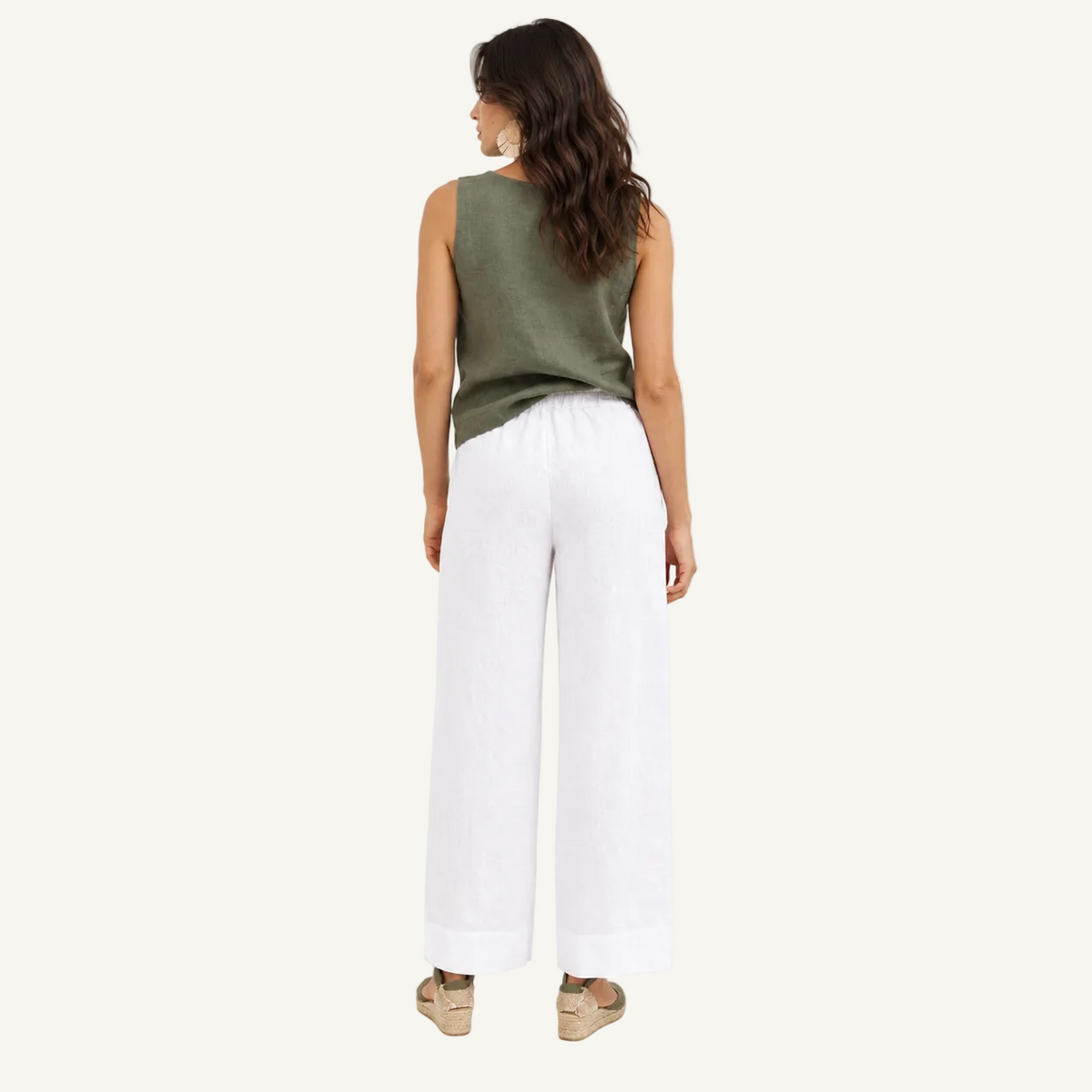 A woman is shown from the back wearing a sleeveless olive green top and white wide-leg pants, standing against a plain white studio background.