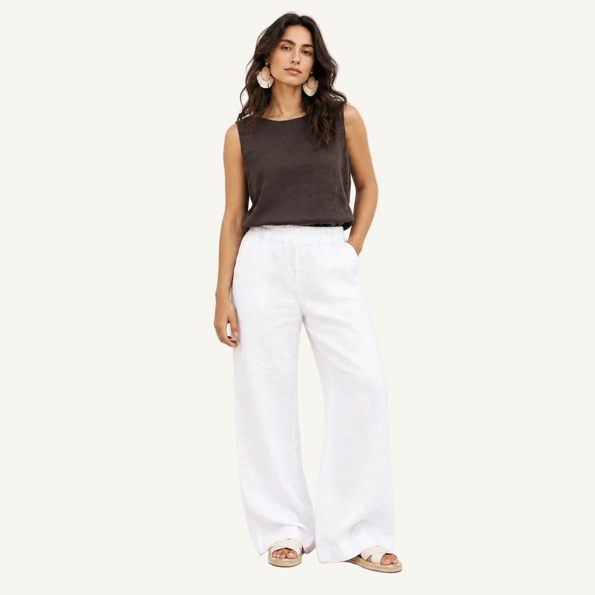 A woman modeling a sleeveless dark brown top and white wide-leg linen pants against a clean white studio background.