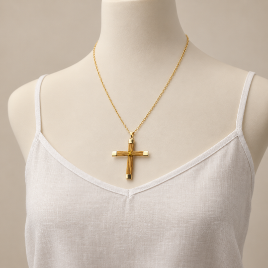 A gold cross pendant necklace on a delicate gold chain, displayed on a white mannequin torso wearing a white camisole top against a warm beige background.