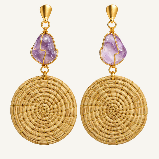 A pair of gold-toned dangle earrings featuring a large round woven raffia disc and a bezel-set purple amethyst stone above it, shown on a clean white background.