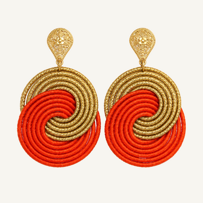 A pair of statement dangle earrings featuring textured gold metal filigree studs and large circular disc elements in alternating metallic gold and bright orange-red cord, set against a plain white background.