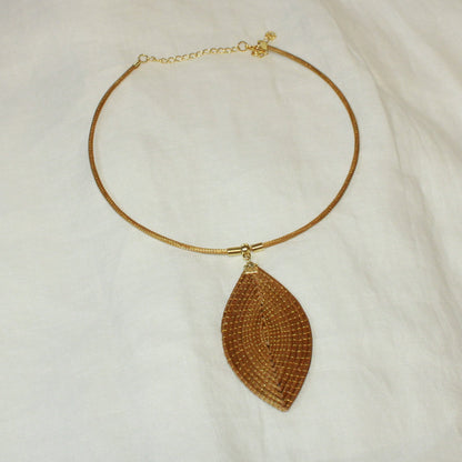 Vida Folha Dourada Necklace handcrafted from Golden Grass featuring a woven leaf-shaped pendant on a gold-tone chain.